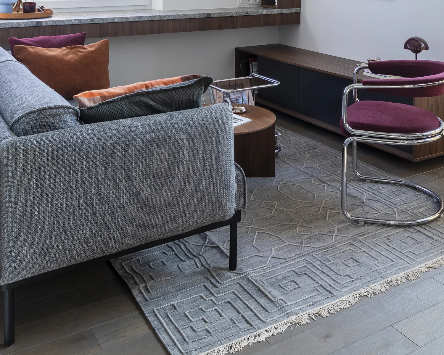 Illustratives Beispiel: Wohnraum mit grauem Sofa, Teppich und Nussbaum-Sideboard